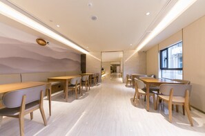 A modern interior with wooden tables and chairs, a light-colored floor, and a view through a doorway. - Ji Hotel (Nanjing)