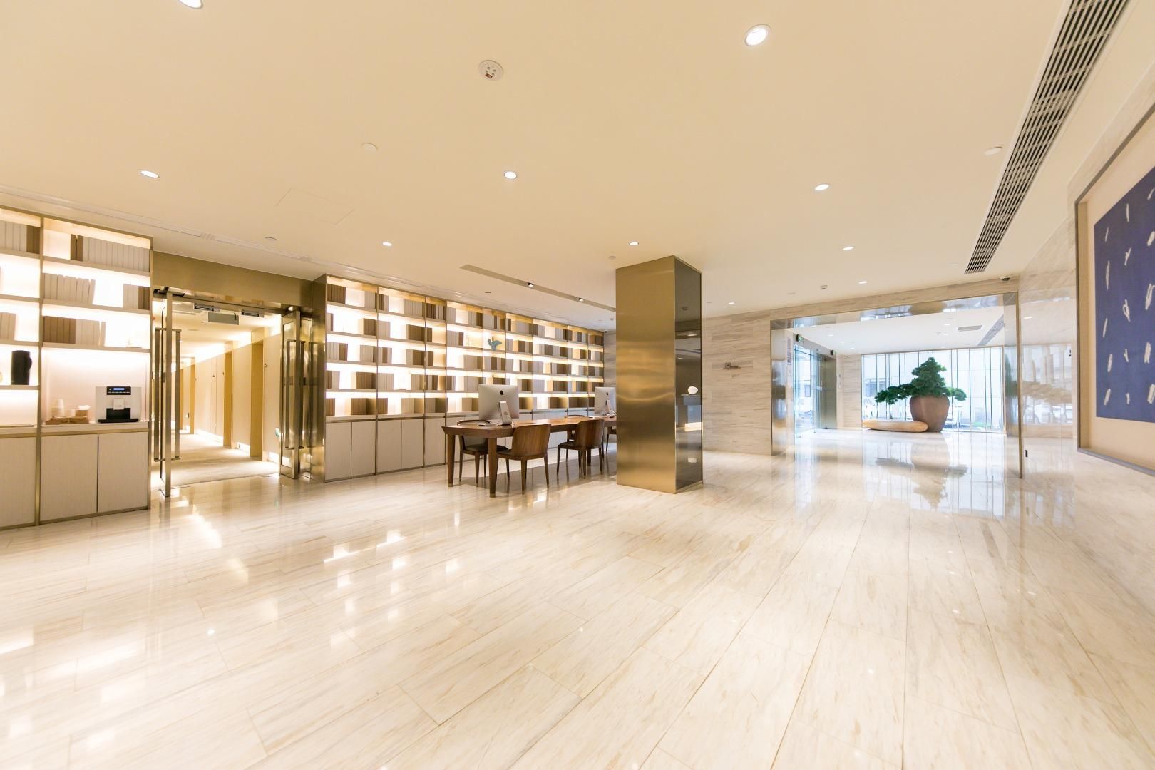 A spacious lobby with a modern design, featuring a long reception desk, a seating area, and a large potted plant.