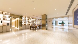 A spacious lobby with a modern design, featuring a long reception desk, a seating area, and a large potted plant. - Ji Hotel (Nanjing)