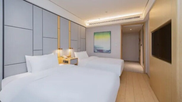 A hotel room with a large bed, bedside tables, a TV, and a painting on the wall. - Ji Hotel (Nanjing)
