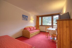 A room with a single bed, a sofa, a small table with chairs, and a window with curtains.