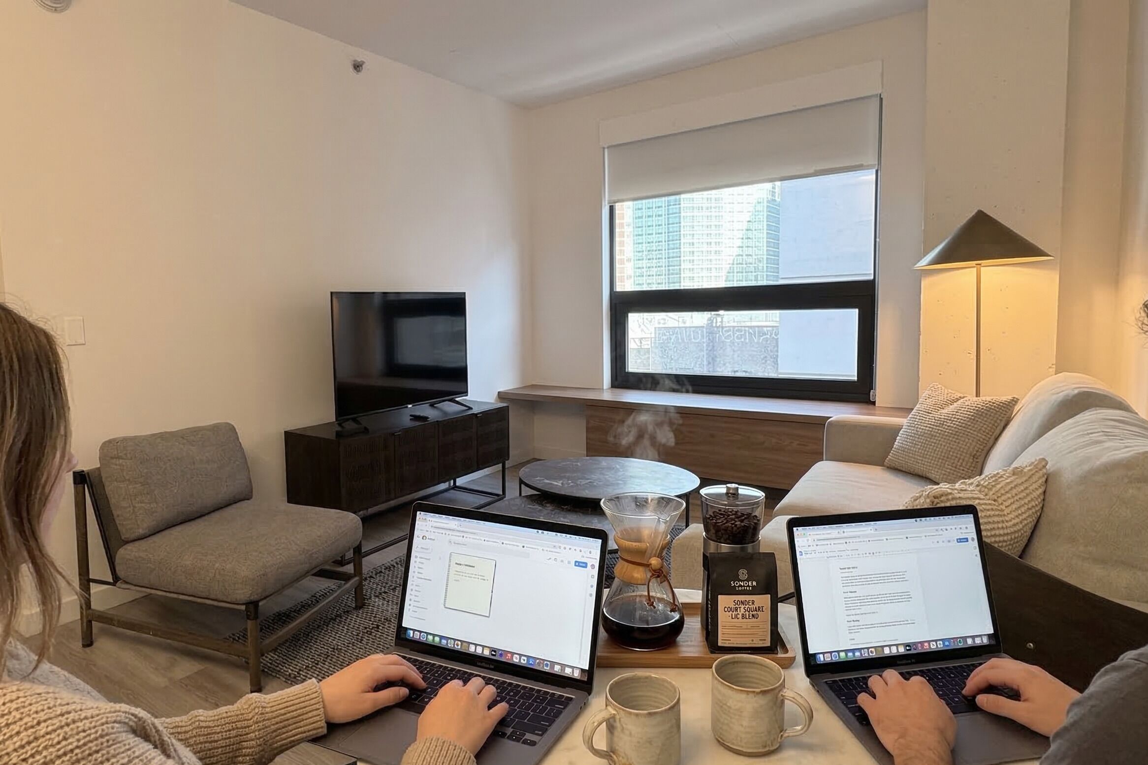 A modern living room with two laptops, a coffee maker, and a television.