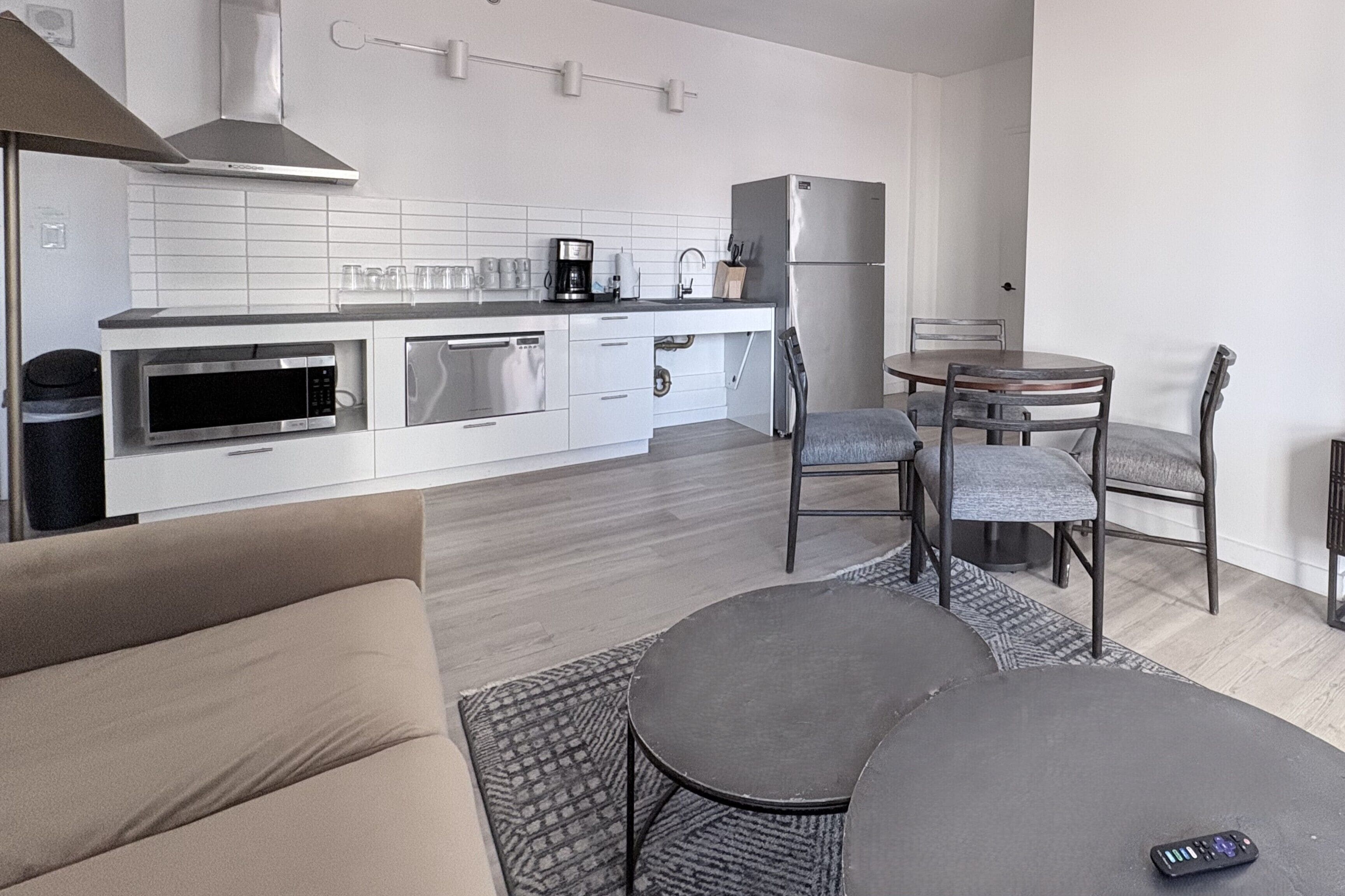 A modern kitchen with a dining area, including a sofa, a round table, and a remote control on the table.