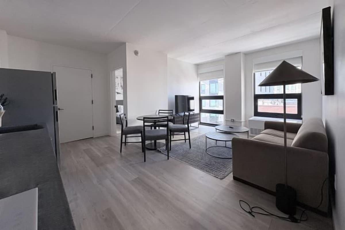 A modern living room with a sofa, a coffee table, a TV, and a dining area with chairs and a table.