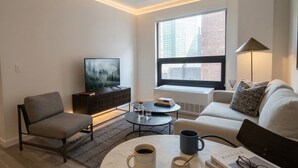 A modern living room with a sofa, armchair, coffee table, and a TV. - Court Square Hotel Long Island City New York , Belvilla District 6 Formerly Sonder (Long Island City)