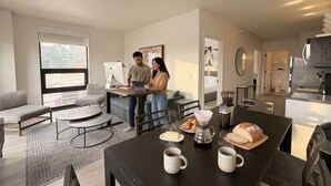 A modern living room with a sofa, coffee table, and dining table with food and drinks. - Court Square Hotel Long Island City New York , Belvilla District 6 Formerly Sonder (Long Island City)