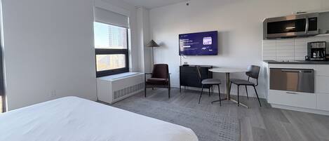 Ein Hotelzimmer mit Bett, Schreibtisch, Stuhl, Fernseher und einer Küchenzeile.