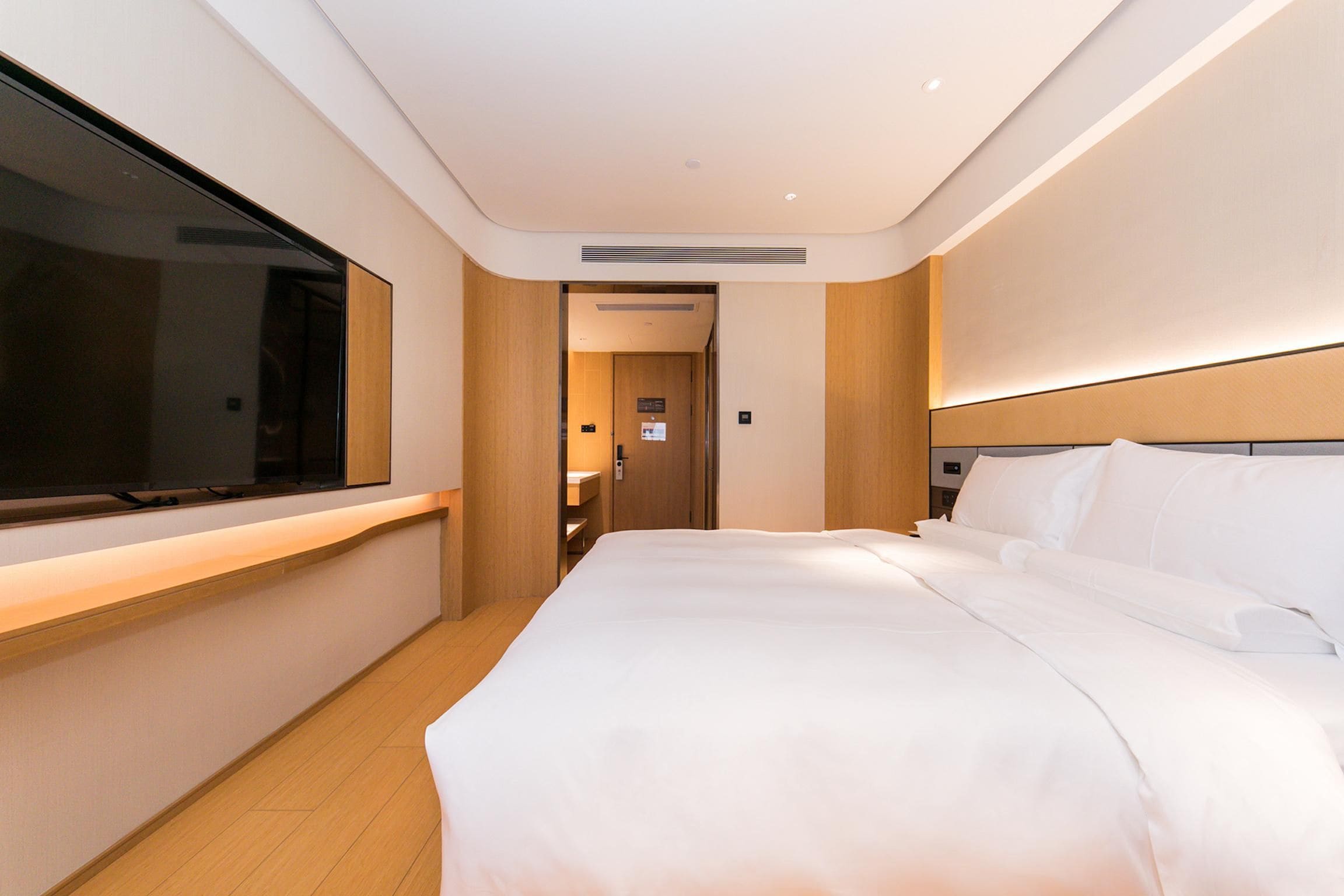 A hotel room with a large bed, a TV mounted on the wall, and a wooden floor.