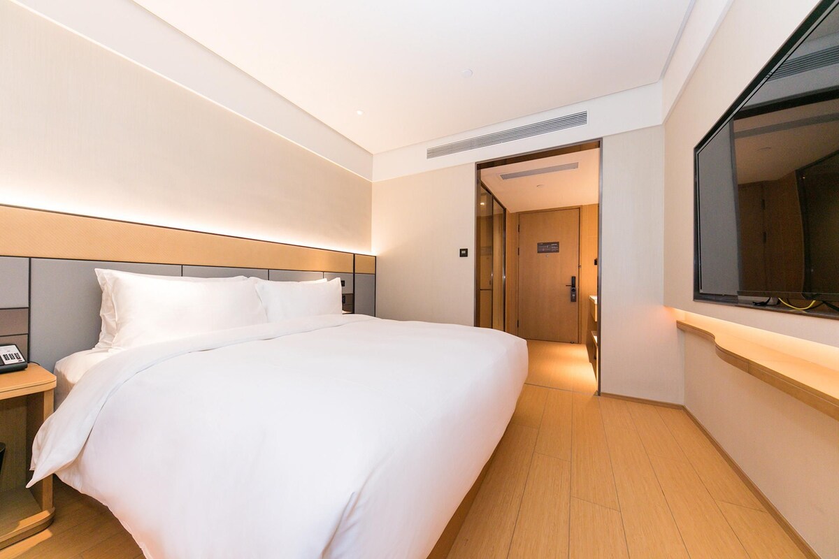 A hotel room with a large bed, bedside table, and a window.