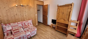 Una habitación acogedora con piso de madera, un sofá estampado, un armario de madera y un televisor.