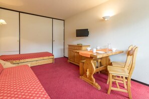 A room with a bed, a desk with a chair, a television, and a red carpet.