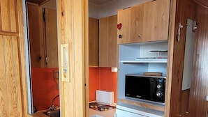 Une cuisine de taille réduite, dotée de meubles en bois, d’un réfrigérateur blanc et d’un four à micro-ondes placé sur le dessus.