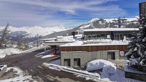Un bâtiment moderne, avec un télésiège et des montagnes enneigées en arrière-plan.