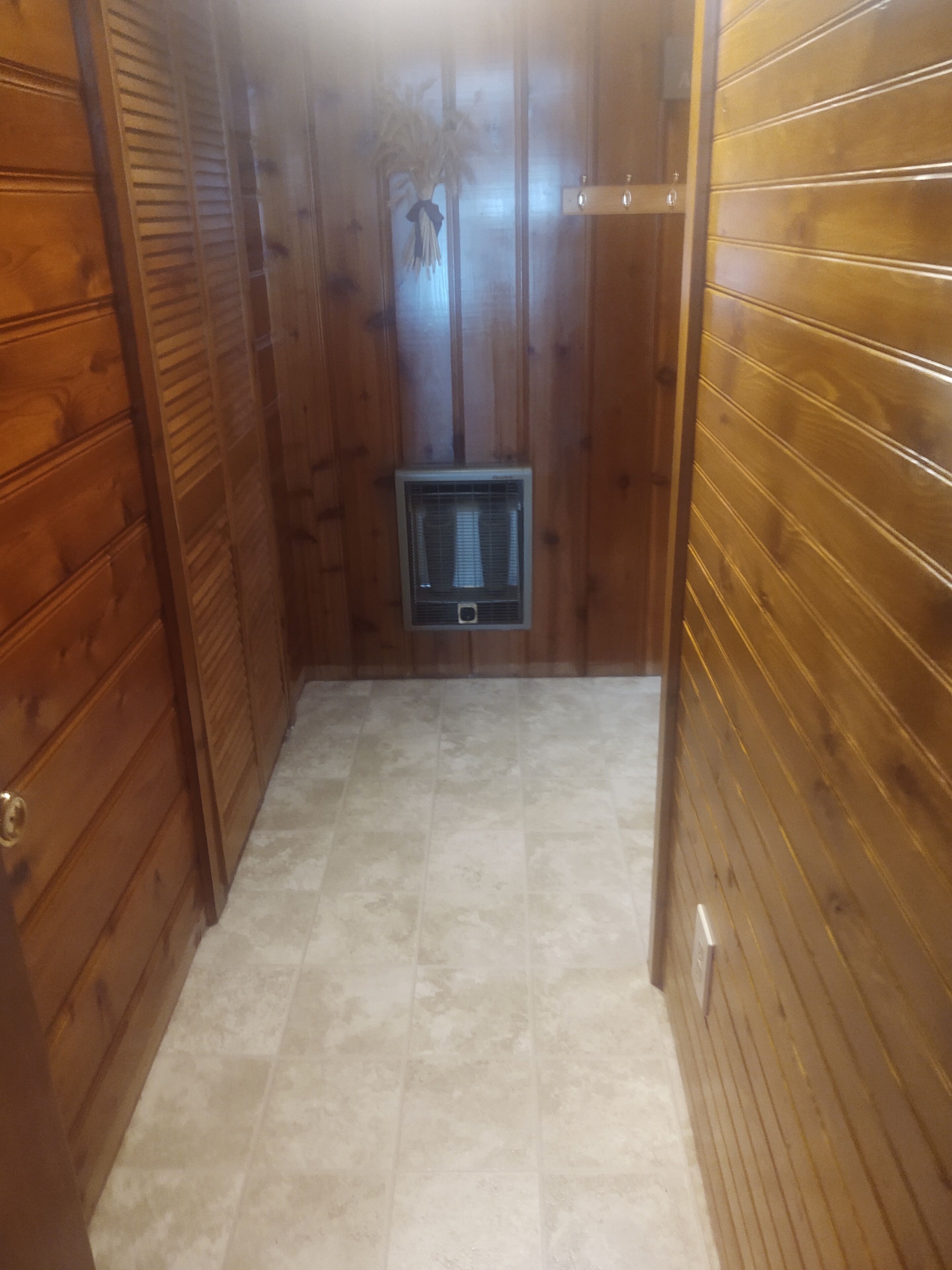 A narrow hallway with wooden paneling on the walls and a tiled floor. A small air conditioning unit is mounted on the wall in the center.