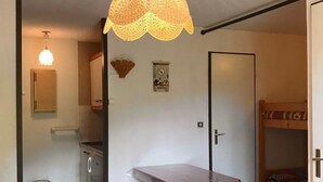 Un espacio habitable compacto con un banco de madera, una mesa, una lámpara colgante, una pequeña cocina y una cama litera.