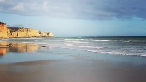 Een strand met een rustige zee, een zandstrand en kliffen op de achtergrond.