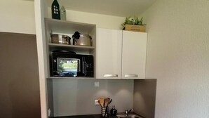 Une cuisine compacte équipée d’un four à micro-ondes, d’un petit évier et d’un lave-vaisselle. On y trouve des placards au-dessus du plan de travail et une petite plante posée sur l’étagère supérieure.