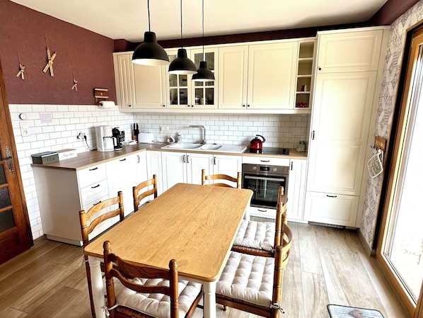 A kitchen with white cabinets, a wooden table, and hanging pendant lights. - Gîte "Le Lupulus", space and comfort 10' from Gerardmer (Le Tholy)