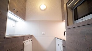 A compact kitchen with wooden cabinets, a built-in dishwasher, and a microwave. - 200m from ski slopes, 1st floor, view ski slopes, balcony, tv, ski locker, 27m², Valmorel (Valmorel)