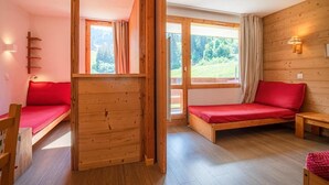 A cozy room with wooden walls and floors, featuring two red beds and a wooden bench. - 200m from ski slopes, 1st floor, view ski slopes, balcony, tv, ski locker, 27m², Valmorel (Valmorel)