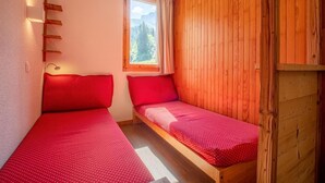 A small room with two single beds, wooden walls, a window with a view of trees, and a wall-mounted shelf. - 200m from ski slopes, 1st floor, view ski slopes, balcony, tv, ski locker, 27m², Valmorel (Valmorel)