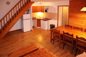A wooden staircase leading to a kitchen with a dining area below.
