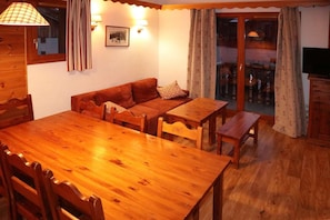A cozy room with a wooden dining table, two sofas, and a small wooden table. There are two wall-mounted lamps and a framed picture on the wall. - Ski-in/ski-out & foot of the slopes, 3rd floor, swimming pool, sauna, balcony, tv, ski locker, 61m² (Les Orres)
