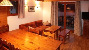 Una habitación acogedora con una mesa de comedor de madera, dos sofás y una pequeña mesa de madera. Hay dos lámparas de pared y un cuadro enmarcado en la pared.