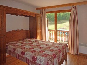 A bedroom with a wooden four-poster bed, a balcony with curtains, and a view of a grassy area.
