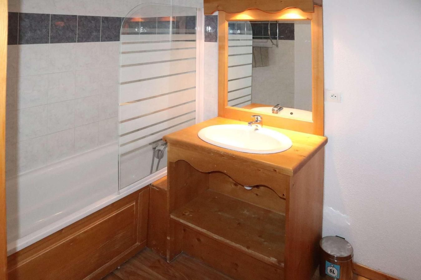 Une salle de bain avec un meuble-lavabo en bois, un lavabo blanc et une cabine de douche en verre.