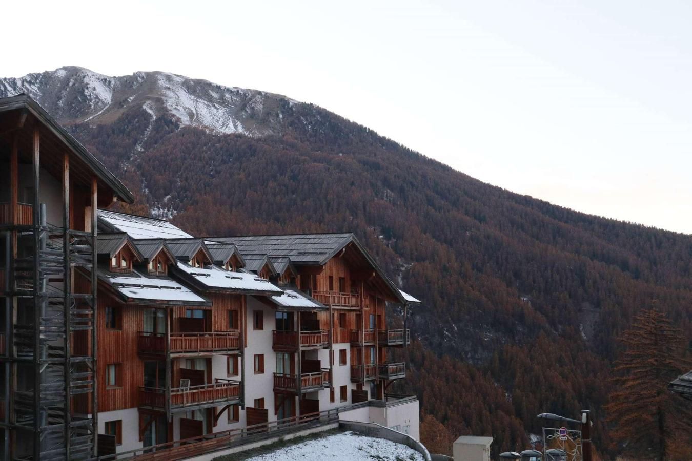 Un bâtiment de style chalet en bois, doté de nombreux balcons, qui se dresse sur un fond de paysage montagneux.