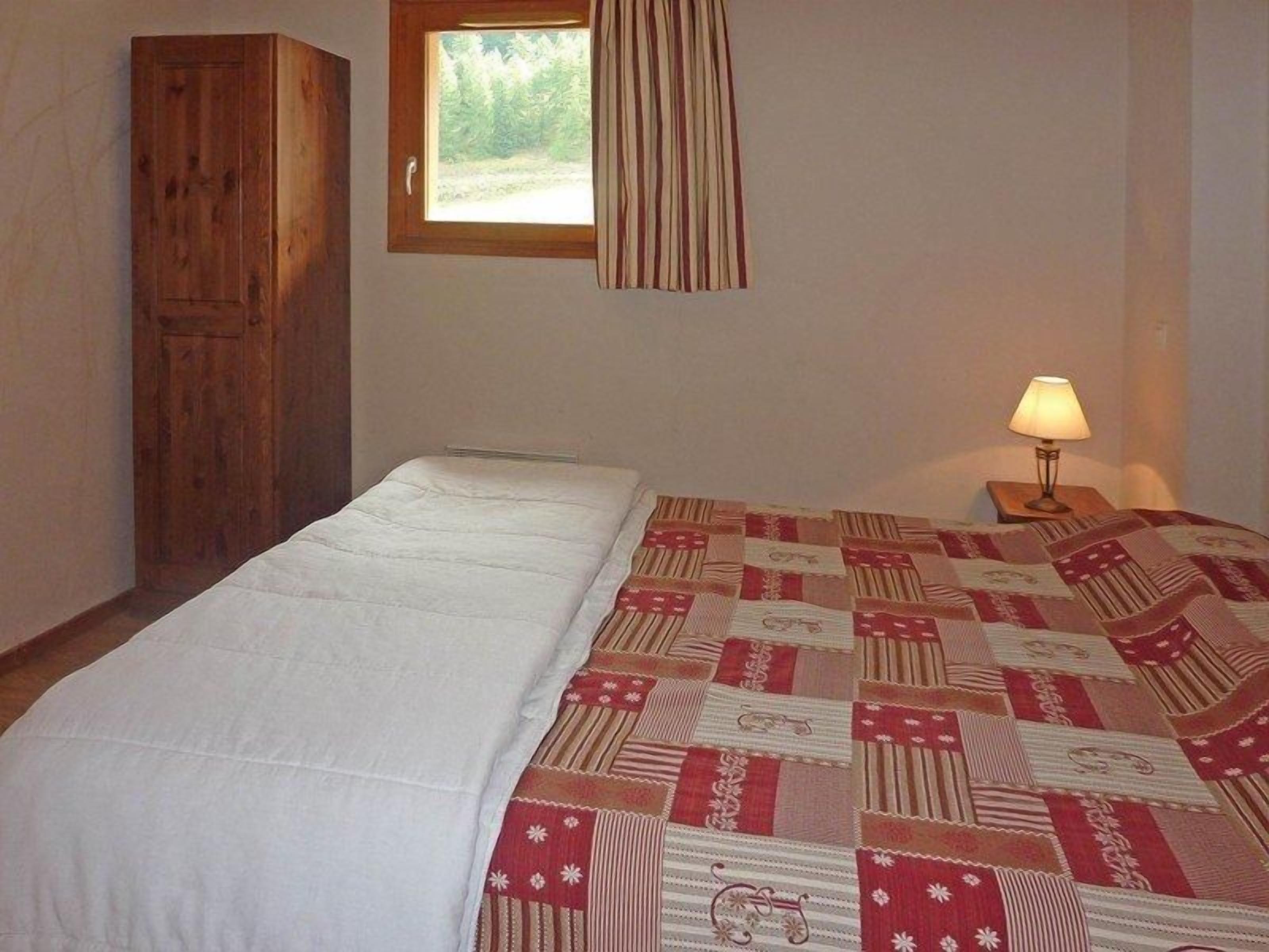 Une chambre à coucher avec un lit, une armoire en bois, une fenêtre avec des rideaux et une lampe de chevet.
