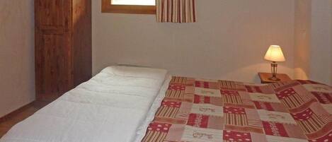 Un dormitorio con cama, armario de madera, ventana con cortinas y lámpara de noche.