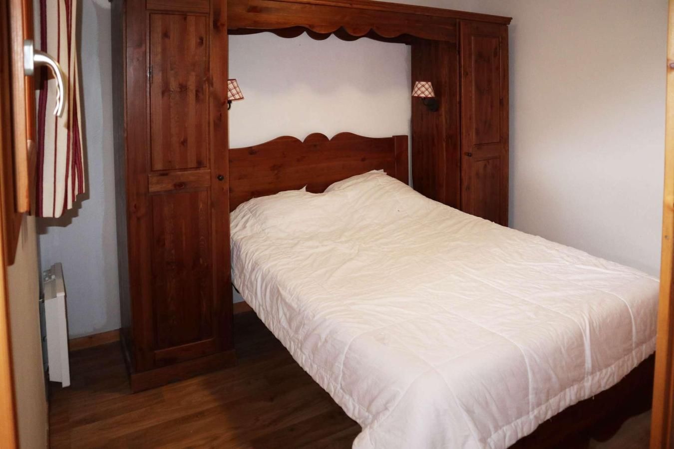 Ein Schlafzimmer mit einem hölzernen Kopfteil, einer weißen Bettdecke und einem Schrank aus Holz mit Spiegel.