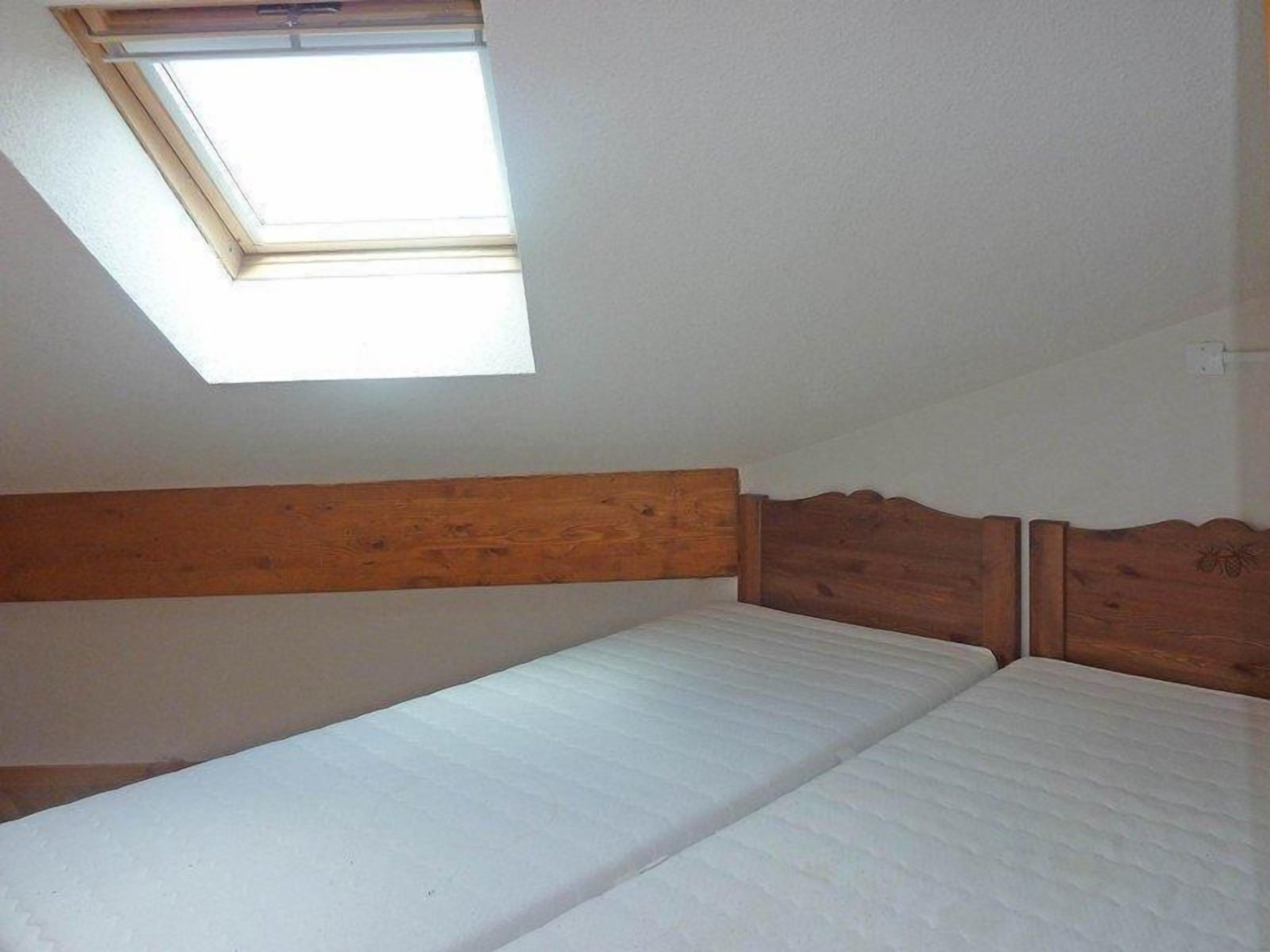 A room with a single bed, wooden headboard, and a skylight.