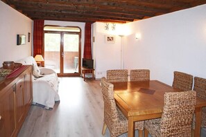 A cozy room with a wooden dining table and wicker chairs, a bed with a red curtain, and a television on a small stand. - 50m from resort center, 5th floor, view resort, balcony, 40m², Les Orres (Les Orres)
