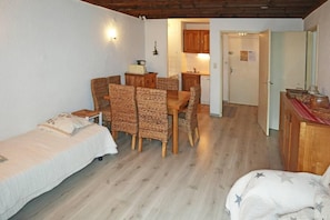 A room with a bed, a dining table with chairs, a kitchen area, and a door.