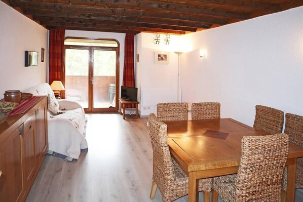 A cozy room with a wooden dining table, wicker chairs, a television, and a sliding glass door leading to an outdoor area.