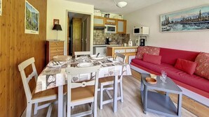 Una sala acogedora con una mesa de comedor para cuatro personas, un sofá rojo y una cocina al fondo.