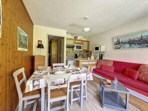 Ein gemütlicher Wohnbereich mit einem Esstisch für vier Personen, einem roten Sofa und einer Küche im Hintergrund.