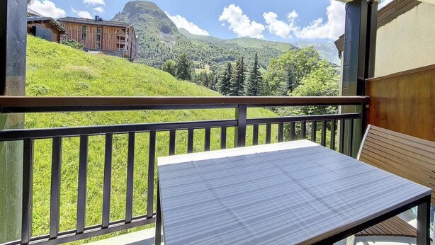 Un balcón con mesa y banco, con vistas a un paisaje montañoso y un edificio al fondo.
