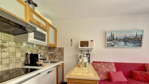 Cocina compacta con microondas, hervidor, cafetera, una isla de madera y un sofá rojo con cojines estampados.