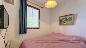 Un dormitorio con cama, ventana con cortinas, un cuadro en la pared y una lámpara en el techo.