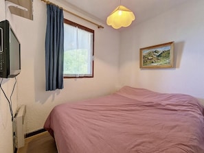 Ein Schlafzimmer mit Bett, einem Fenster mit Vorhängen, einem Bild an der Wand und einer Deckenleuchte.