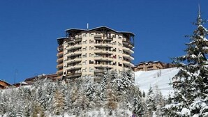 Un hotel a più piani con balconi, circondato da alberi innevati e un cielo azzurro limpido.