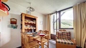Zona pranzo con tavolo e sedie di legno, un mobiletto contenitore con stoviglie e un divano a quadri.