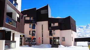 En moderne bygning med mange etager, altaner og et skiområde i baggrunden.