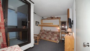 Et lille hotelværelse med køjeseng, skrivebord med lampe, fjernsyn og vindue med udsigt.