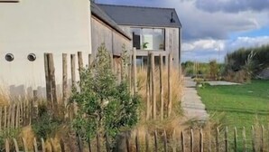 A modern house with a large window, a wooden fence, and a grassy yard.