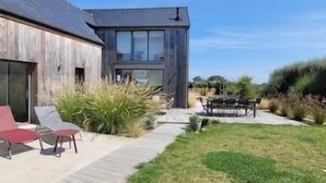 A modern house with a large glass door, a patio with two red chairs, and a grassy yard.